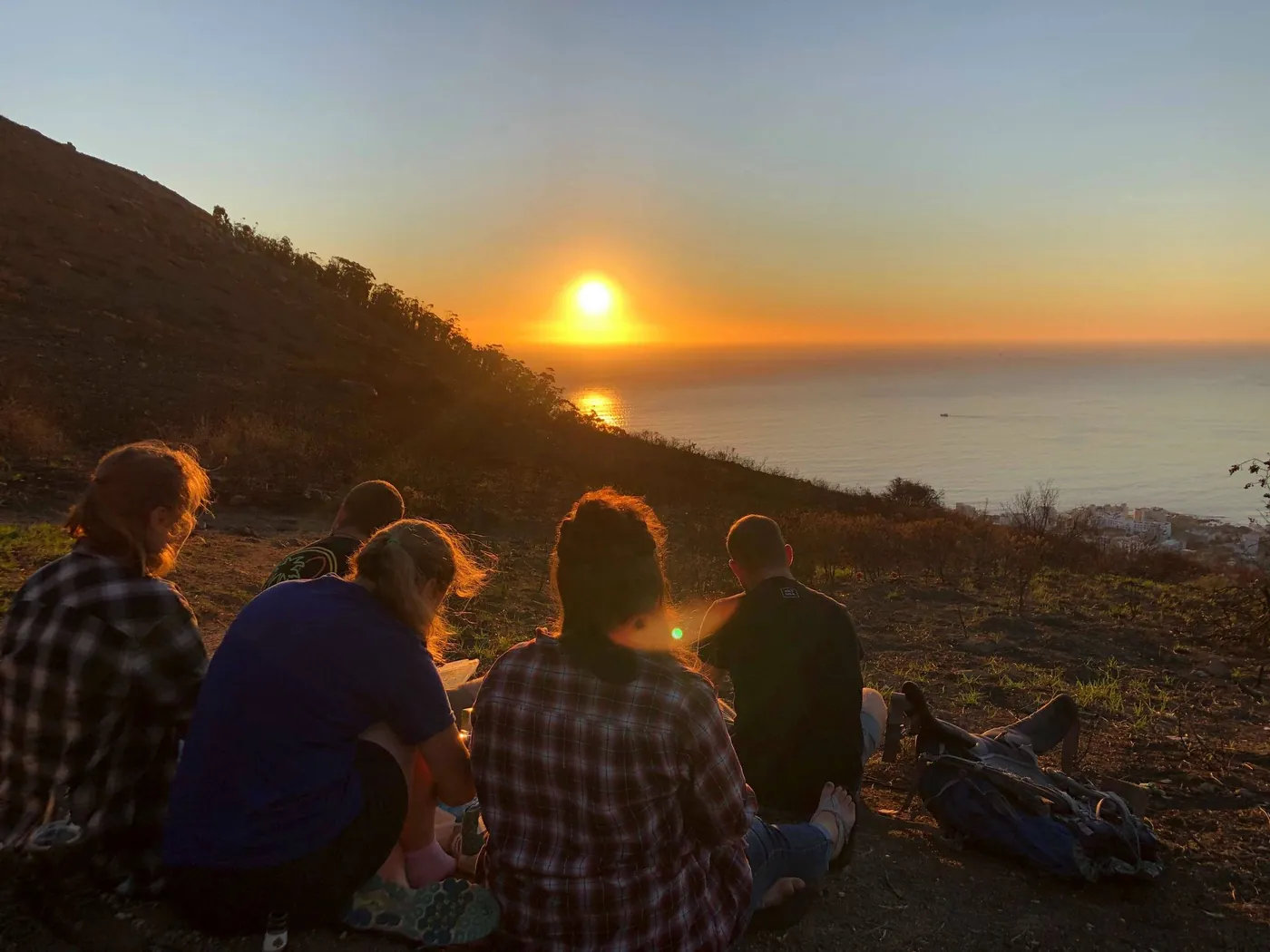 Young people watching the sunset over the sea from a hillside