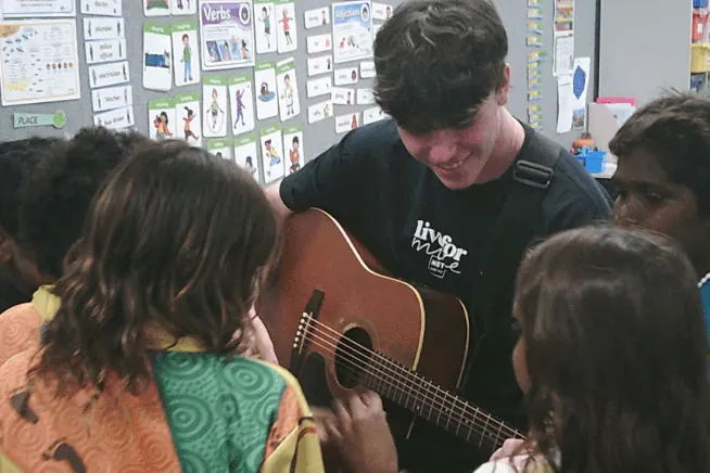 A NET team member with a guitar and students in a classroom