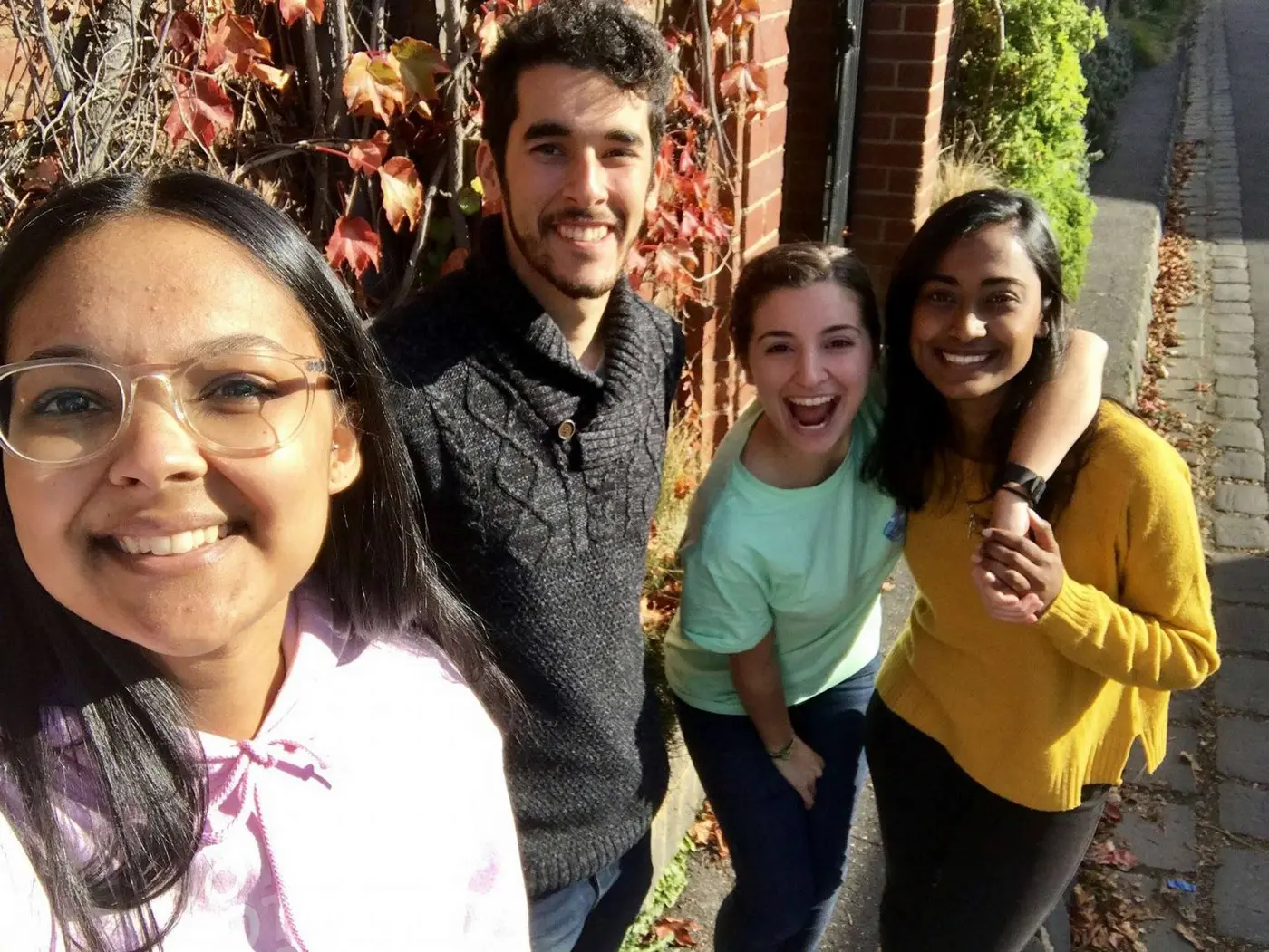 Four young people smiling outdoors beside a brick wall