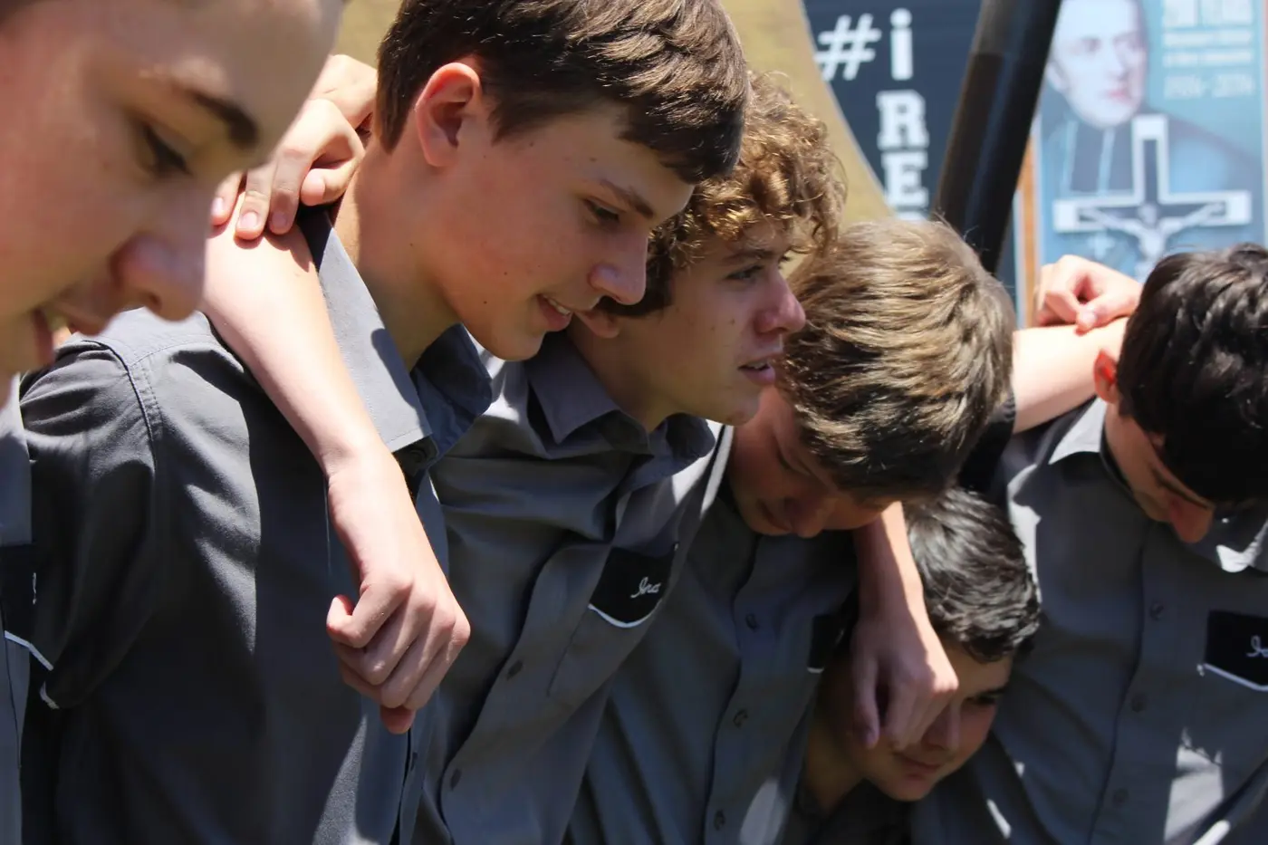 Schoolboys in grey shirts with their arms around each other