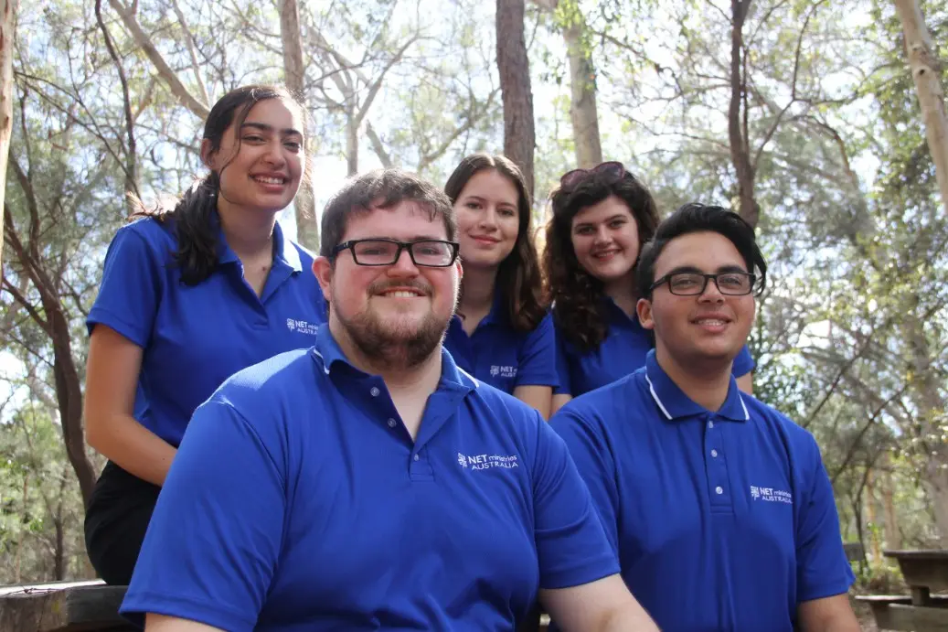 Five NET missionaries in blue shirts among the trees