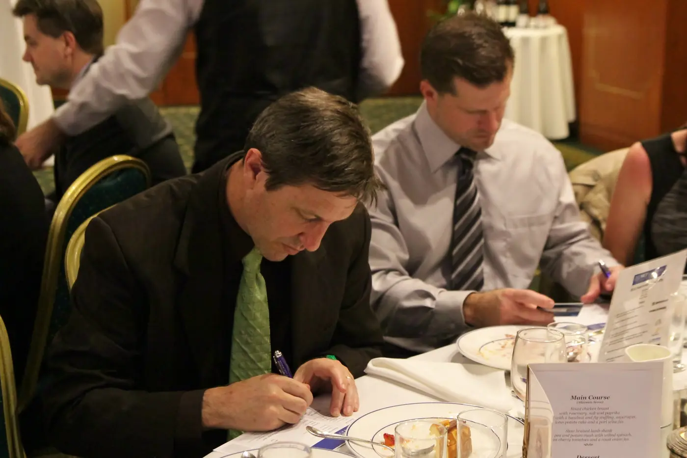 Men in shirts and ties filling in forms at a dinner table