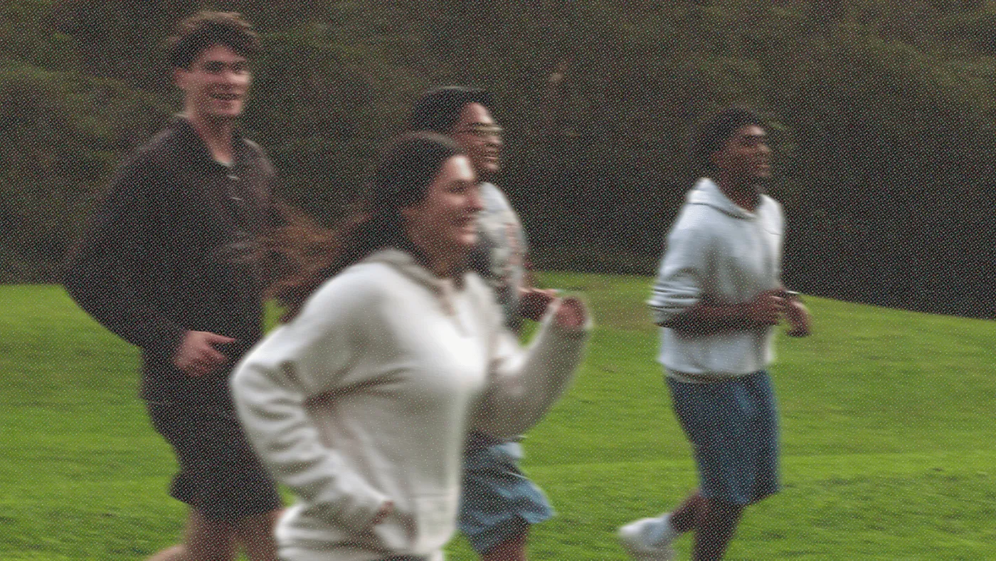 Four young people running across a green field