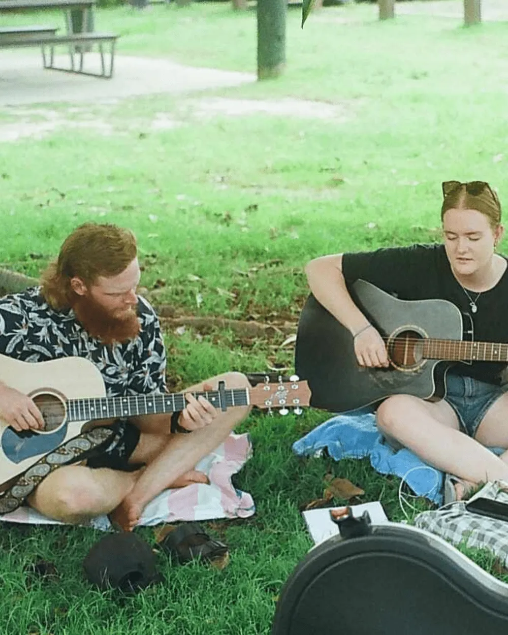 Two people playing guitar on the grass