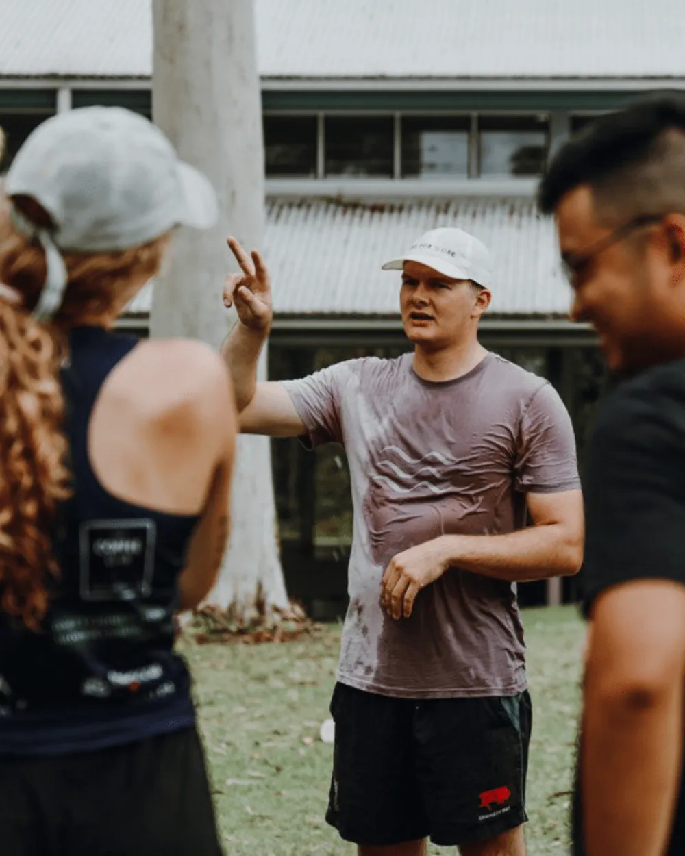 A man in a cap talking with two young people outdoors
